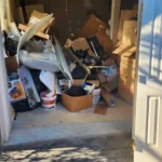 Cluttered garage filled with boxes, furniture, and household junk for cleanout